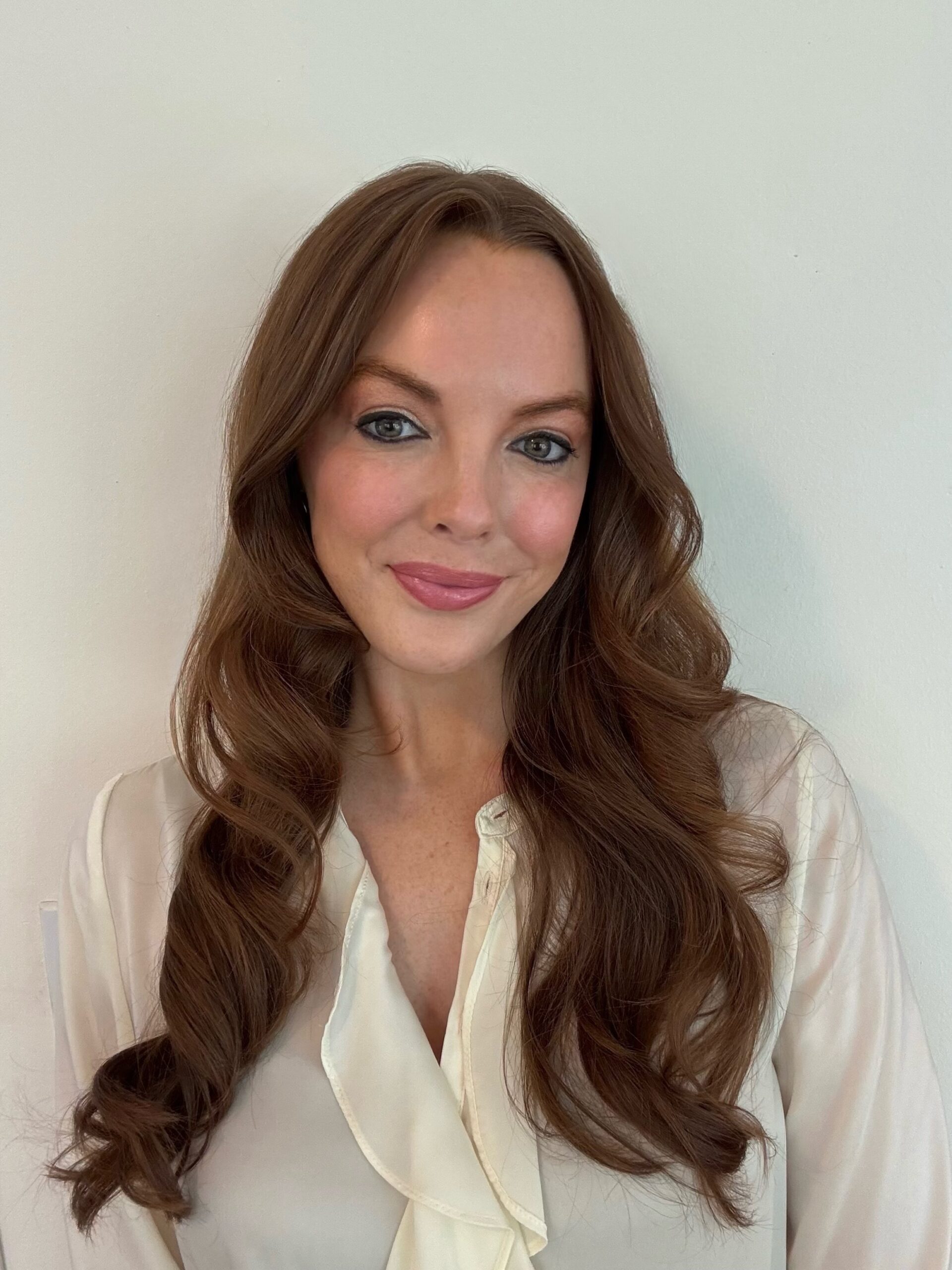 Smiling woman with wavy brown hair wearing a white blouse.