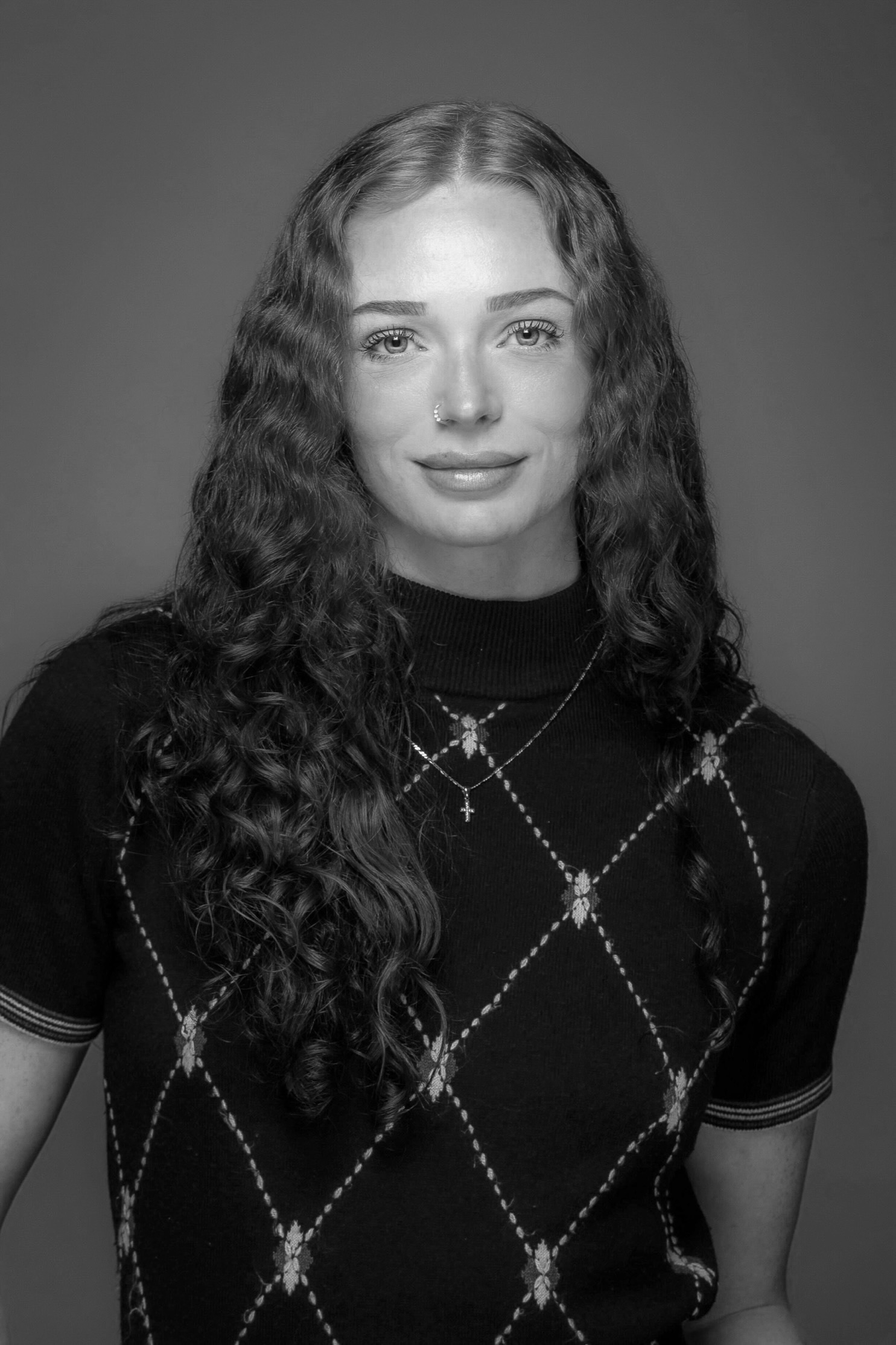Black and white portrait of a woman with long curly hair and a patterned sweater.