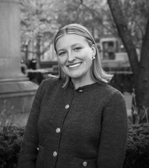 Smiling woman in a dark buttoned coat outdoors.