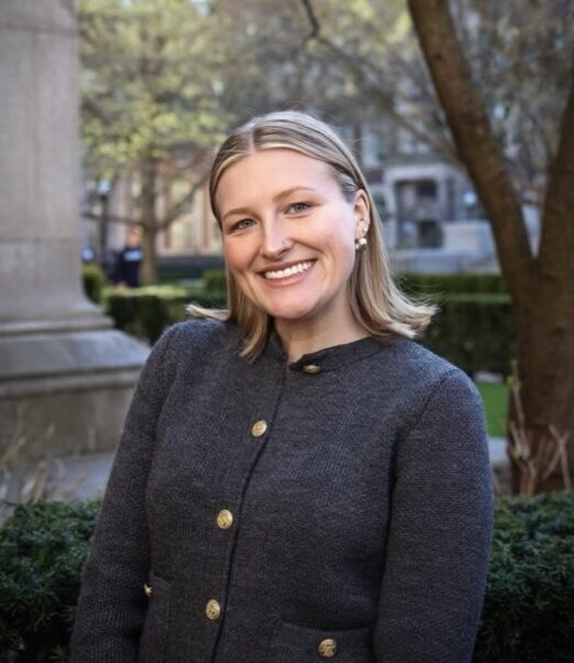 Smiling woman in a dark coat outdoors in a park.
