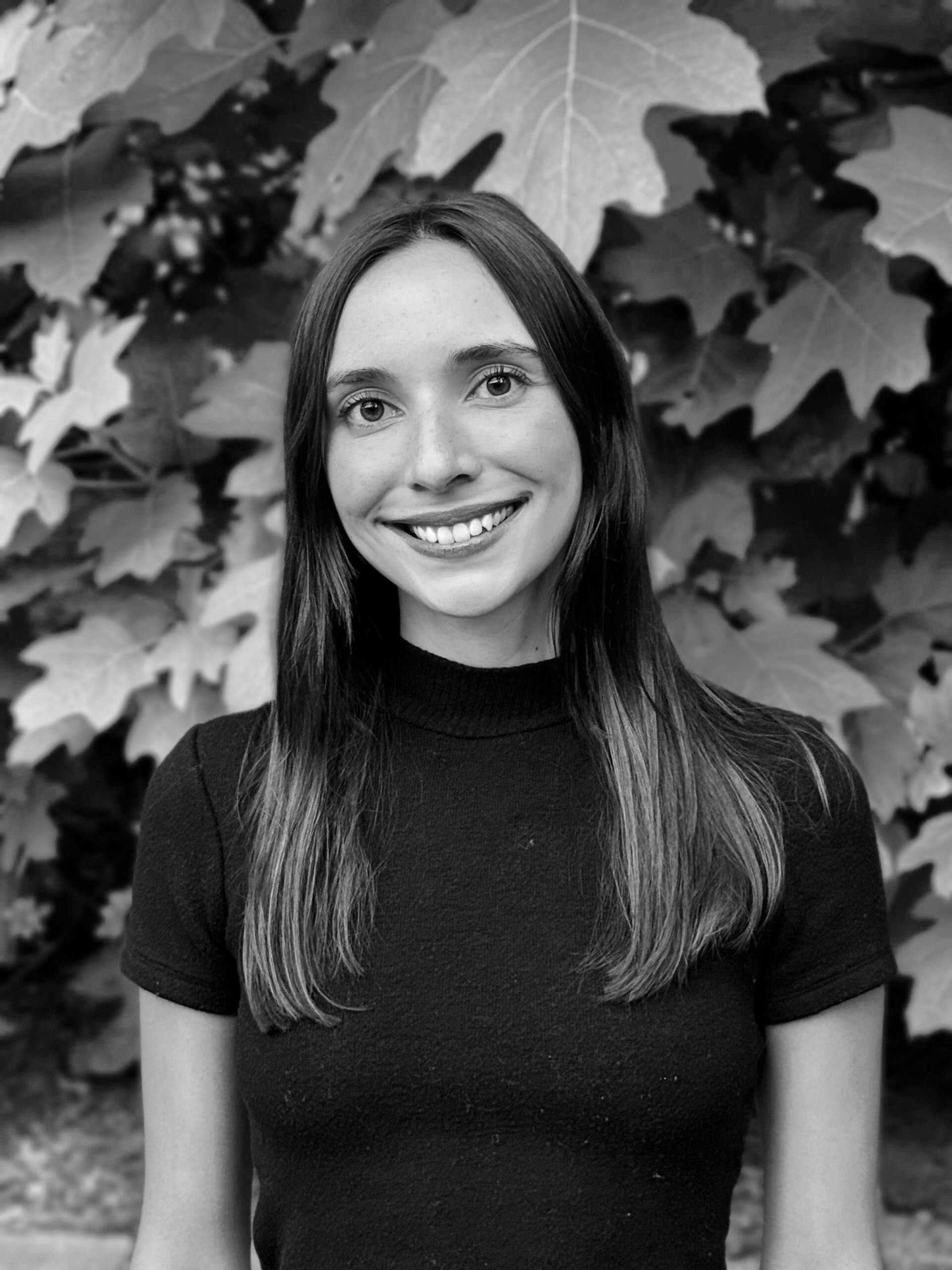 Smiling woman with long hair in front of leafy background.