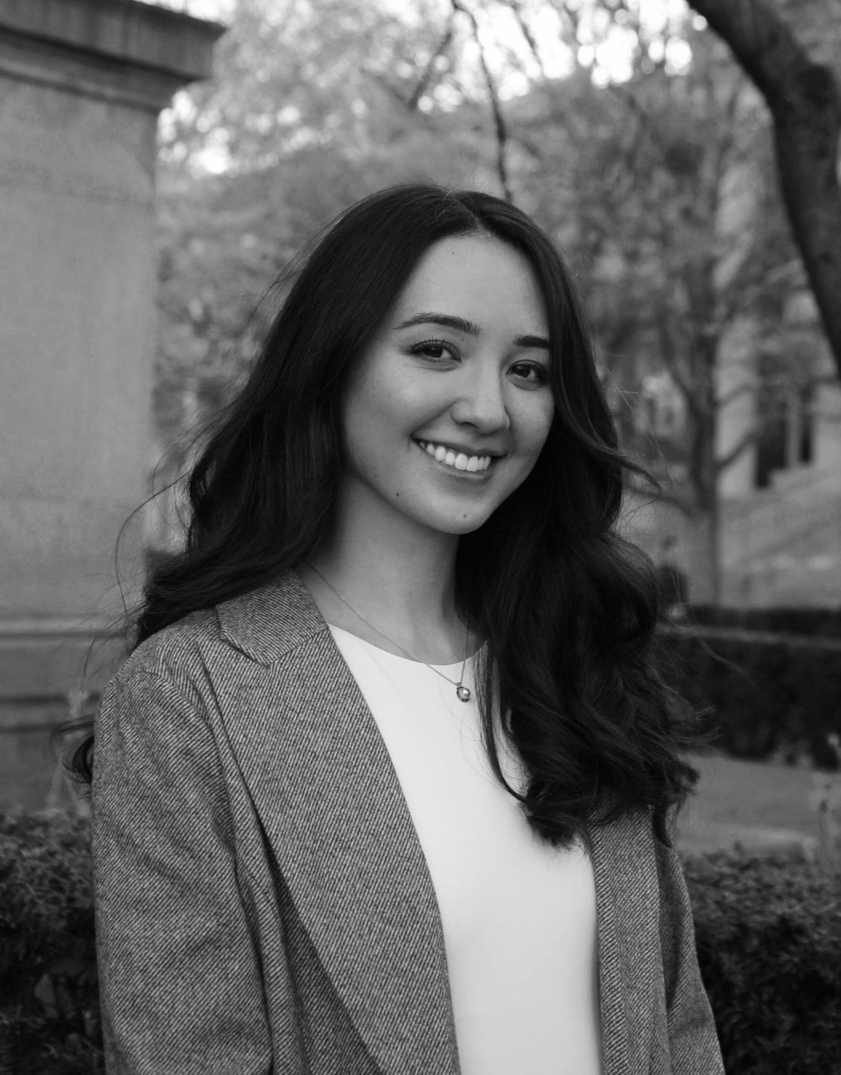 A smiling woman with long hair in a gray blazer outdoors.